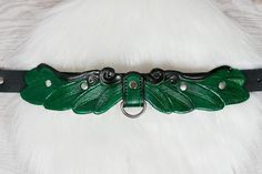 a green leather belt with leaves and metal buckles on a white fur coat background