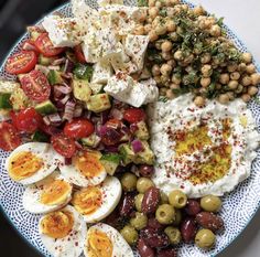 a blue and white plate topped with eggs, tomatoes, olives, cucumbers and other foods