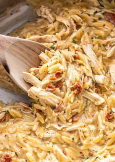 a wooden spoon in a pasta dish with chicken and tomatoes