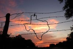 a barbed wire fence with the sun setting behind it