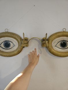 a person's hand is reaching up towards two eye shaped mirrors on the wall