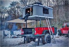 a man sitting on top of a red truck in the snow next to a camper