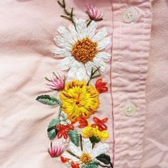 a pink shirt with white and yellow flowers embroidered on the chest, along with green leaves