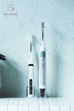 two electric toothbrushes sitting next to each other on top of a white counter