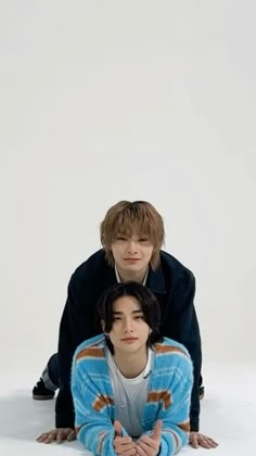 two young men sitting next to each other in front of a white background, one with his head on the floor