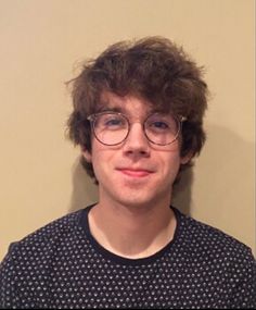 a young man with glasses is smiling for the camera while standing in front of a wall