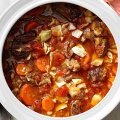 a pot filled with stew and vegetables on top of a table next to a pine cone