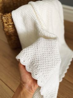 a person holding up a white blanket on top of a wooden floor next to a wicker basket