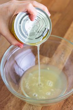 a person pouring something into a bowl with some liquid in it on a wooden table