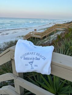 a white pillow sitting on top of a wooden bench next to the ocean and beach