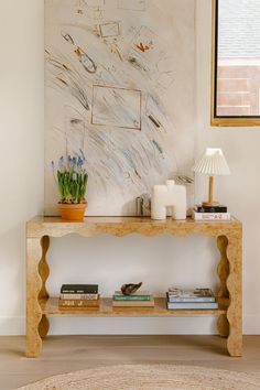 a wooden table with books and plants on it in front of a large art piece