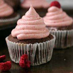 three cupcakes with pink frosting and raspberries on the top one