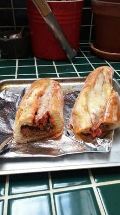 two sandwiches sitting on top of tin foil covered in cheese and meat, next to a potted plant