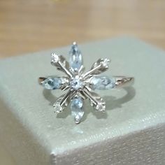 a ring is sitting on top of a white box with blue stones in the shape of a snowflake