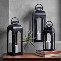 three black lanterns on a table with an air plant in the middle and one lit