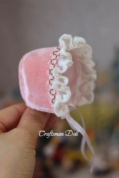 a hand holding a pink heart shaped object with white lace on it's edge