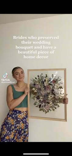 a woman holding up a framed photo with flowers on it and the words brides who preserved their wedding bouquet and have a beautiful piece of home decor