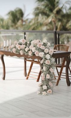 a table with flowers and candles on it next to a wooden bench in front of palm trees