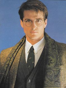 a man wearing glasses and a suit with a scarf around his neck is looking at the camera