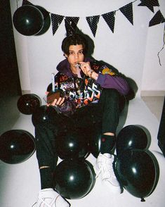 a young man sitting on the floor with balloons and confetti in his mouth