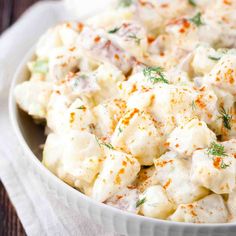 a white bowl filled with potato salad on top of a wooden table