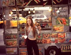 a woman standing in front of a food truck holding a doughnut and posing for the camera