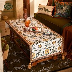 the table is covered with an intricately designed cloth and sits in front of a couch