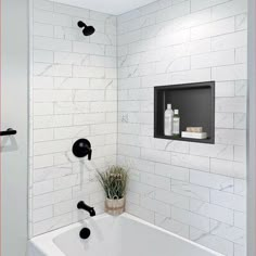 a bathroom with white tile and black faucet shower head in the bathtub