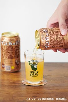 a person pouring beer into a glass on top of a wooden table next to a can