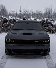 the front end of a black car parked on top of a snow covered parking lot