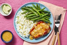 a blue plate topped with meat, rice and green beans next to a bowl of sauce