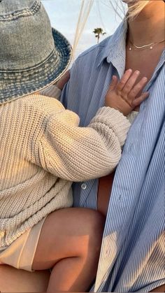 a woman holding a baby in her arms while wearing a blue shirt and tan shorts