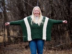 a woman standing in the woods with her arms spread out and she is wearing a green sweater