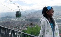 a woman standing in front of a cable car on top of a hill next to a city