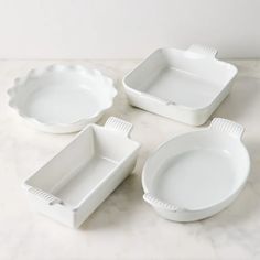 four white dishes sitting on top of a marble counter next to each other and one empty dish