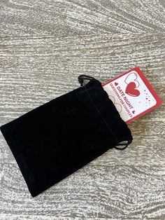 a black velvet pouch sitting on top of a wooden table next to a red and white tag