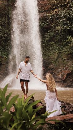 a man and woman holding hands in front of a waterfall