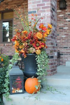 an arrangement of flowers and pumpkins sits on the front steps of a brick house