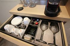 an open drawer with utensils and other items in it on top of a table