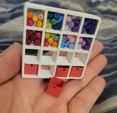 a hand holding a small toy with different colored beads in it's display case