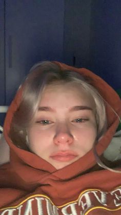 a woman with blonde hair wearing a red hoodie and looking at the camera while she has her eyes closed