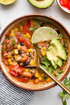 a bowl filled with mexican chicken soup next to sliced avocado and cilantro