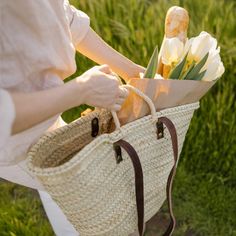 a woman holding a straw bag with flowers in it and some sand on the ground