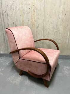 a pink chair sitting on top of a cement floor next to a wooden framed wall