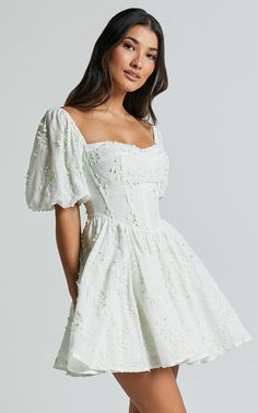 Celebrate the beauty of spring with our Esthela Mini Dress in Pale Mint. This enchanting piece features an embroidered square neck and short puff sleeves, giving it a sweet and feminine look. The corset detail cinches your waist for a flattering fit, while the flowy fit-and-flare silhouette adds a touch of romance to your outfit. Made from soft cotton fabric, this dress is perfect for both day-time parties and special occasions. Embrace your unique style and feel empowered in this gorgeous mini White Dress Classy, Graduation Dress College, Promotion Dresses, Grad Dresses Short, Confirmation Dresses, Cotton Dress Fabric, White Dresses Graduation, Cute White Dress, Short Puff Sleeve