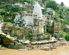 a group of buildings sitting on top of a cliff next to the ocean with umbrellas in front of them