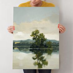 a woman holding up a painting with trees on it