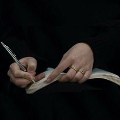 a person holding a pen and writing on a piece of paper in their left hand