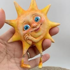 a hand holding a yellow and orange sun brooch with eyes, nose, and mouth