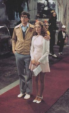 a man and woman standing on a red carpet in front of a building with other people